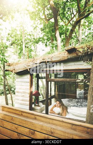 Frau, Kabine und entspannen Sie am Fenster für Reisen, Urlaub oder Aussicht mit Gedanken für Selbstpflege. Weibliche Person, Urlaub oder Resort im Wald mit Ruhe, Pause Stockfoto