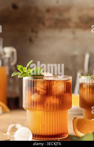 Hummel-Kaffee mit Espresso und Orangensaft in einem Glas mit Eiskugeln und Minze auf braunem strukturiertem Hintergrund mit Textraum. Vertikal Stockfoto