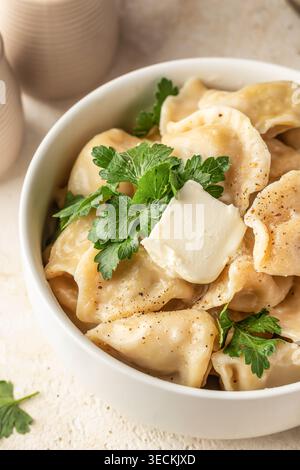 Hausgemachte Fleischknödel oder Pelmeni serviert mit Butter und frischer Petersilie in einer weißen Schüssel. Vertikal Stockfoto