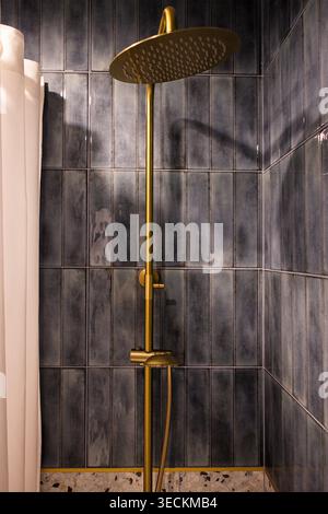 Goldener Duschkopf an der Wand in einem stilvollen Badezimmer mit dunkelblauen Fliesen und einem weißen Duschvorhang in der Ecke Stockfoto