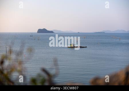 Friedliche Landschaft mit ruhiger, meerferner Insel, kleines Fischerboot, das ruhig über glatte Wasseroberfläche schwimmt, entspannende Atmosphäre unter klarem Licht Stockfoto