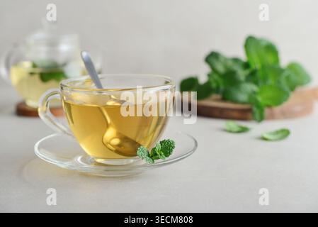Eine Glasschale mit frischem Minztee auf hellem Hintergrund mit einer Teekanne aus Glas und Minzblättern auf einem Holzbrett im Hintergrund. Konzept des gesunden pflanzlichen d Stockfoto