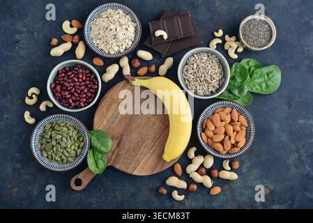Blick von oben auf magnesiumreiche Speisen auf dunklem Hintergrund, einschließlich Hafer, Schokolade, Chiasamen, Sonnenblumen- und Kürbiskerne, Nüsse, Bananen, Spin Stockfoto