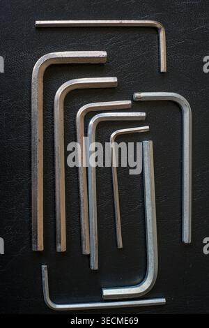Mehrere Sechskantschlüssel aus Metall, auch bekannt als inbusschlüssel, sind in einer flachen Anordnung auf einer dunklen strukturierten Oberfläche angeordnet und zeigen eine Vielzahl von Größen, die für fas verwendet werden Stockfoto
