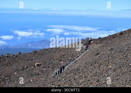 Touristen und Wanderer, die auf einem vulkanischen Steinweg auf den Hängen des Teide wandern und die Inversionsschicht „Mar de Nubes“ (Wolkenmeer) überblicken, Stockfoto