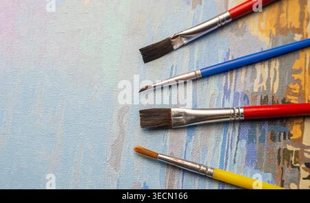 Pinsel in den Farben Rot, Blau und Gelb werden auf einer Leinwand mit bunten Konturen platziert. Der Arbeitsbereich eines Künstlers ist aktiv. Stockfoto