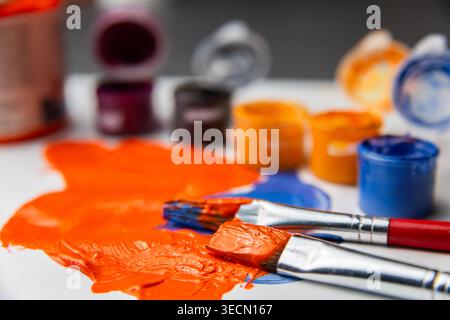 Helle Farbfarben verteilen sich über eine Oberfläche mit Pinseln in der Nähe, die auf die Verwendung in Kunstprojekten und Designs warten. Stockfoto