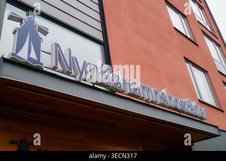 Nynashamnsbostader-Schild am modernen Gebäude Außenwand kombiniert warme Rot- und kühle Grautöne. Nynashamn, Stockholmer County, Schweden, 9. Mai 2025 Stockfoto