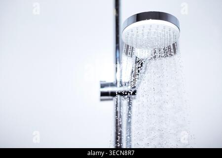 Chrom-Duschkopf gibt einen gleichmäßigen Wasserstrahl in einem modernen Badezimmer ab, das ein minimalistisches Design und eine helle, saubere Ästhetik bietet Stockfoto