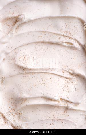 Vanilleeis mit Zimt-Textur, detaillierter Hintergrund. Weicher, gefrorener Joghurt mit Vanille oder Eiscreme mit geriebenen Nüssen aus nächster Nähe. Stockfoto