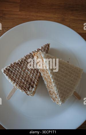 Zwei Waffelkuchen mit Kondensmilch auf einem Stock auf einem weißen Teller. Hausgemachtes Dessert, flach gelegt Stockfoto