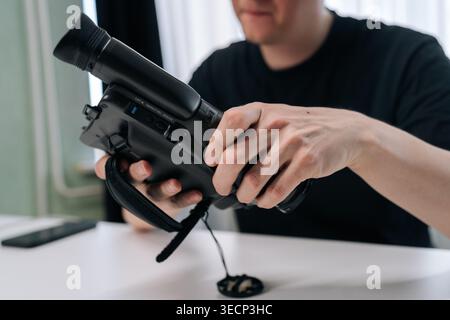 Nahaufnahme von männlichen Händen, die alte schwarze Videokamera bedienen. Person, die an einem weißen Schreibtisch mit sanfter Beleuchtung sitzt. Konzept der Retro-Technik, Nostalgie Stockfoto