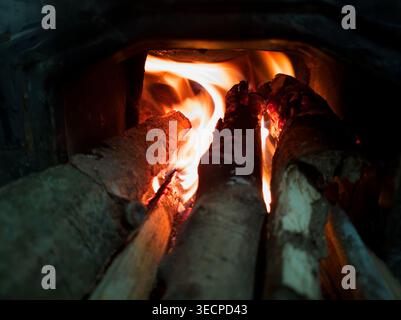 Brennendes Brennholz im traditionellen Holzofen – glühende Flammen und Holzstämme erzeugen Wärme für rustikales Kochen, Nahaufnahme eines Innenfeuers in Kerala Stockfoto