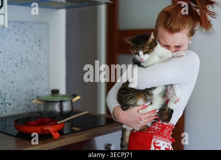 Haustierbesitzerin, die Katze hält, während sie in der Küche Mittagessen macht, warmes Familienkonzept. Stockfoto