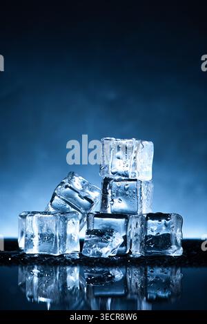 Eiswürfel mit Wassertropfen, die auf einer reflektierenden Oberfläche vor blauem Hintergrund schmelzen Stockfoto