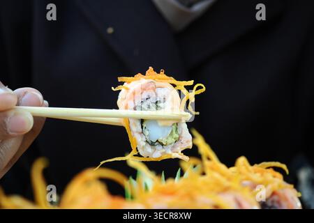 Hand hält Sushi-Rolle mit Stäbchen während einer Mahlzeit Stockfoto