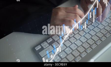 Eine Nahaufnahme der Hände, die auf einer Tastatur mit digitalen Grafiken tippen, die Finanzen und Technologie symbolisieren, in einer modernen professionellen Umgebung Stockfoto
