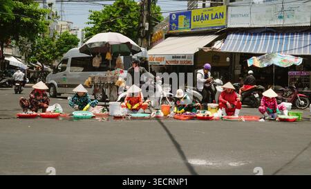 Vietnamesische Straßenverkäufer, die am Straßenrand sitzen und Meeresfrüchte zubereiten, traditionelle Hüte tragen und die lokale Marktkultur und das tägliche Leben in einem Bus festhalten Stockfoto