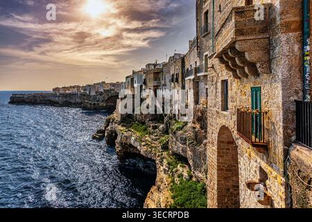 Die historischen weiß getünchten und steinernen Gebäude von Polignano a Mare, hoch oben auf steilen Klippen mit Blick auf das Meer unter einem warmen, bewölkten Himmel. Apulien Stockfoto