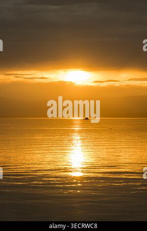 Ein ruhiger Sonnenuntergang über einem ruhigen Meer, in goldenen Tönen während der magischen goldenen Stunde. Das Sonnenlicht reflektiert sich auf dem Wasser und schafft eine ruhige Erbse Stockfoto
