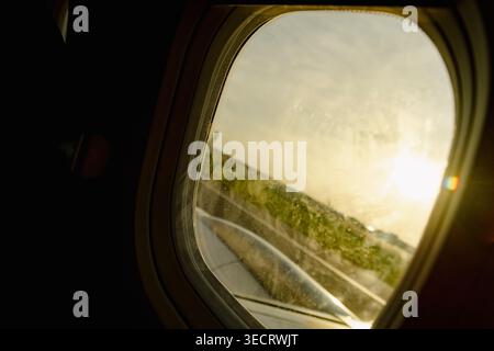 Blick durch ein Flugzeugfenster während des Starts, zeigt den Flügel und die Start- und Landebahn mit goldenem Sonnenaufgangslicht, sanften Reflexen und einer Reisestimmung von innen Stockfoto