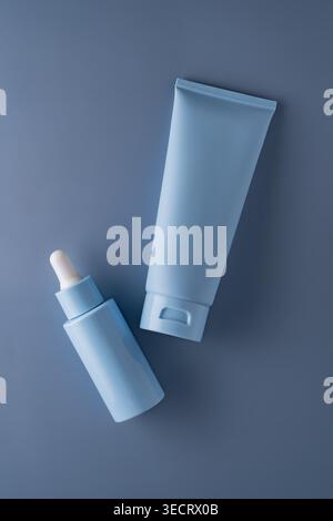 Minimales kosmetisches Modell mit pastellblauer Serumflasche mit Tropfer und passender Creme-Tube auf grauem Hintergrund, ideal für Hautpflege-Branding, p Stockfoto