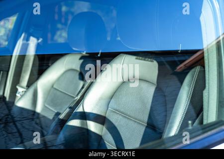 Nahaufnahme der modernen Vordersitze und des Armaturenbrettbereichs durch die Windschutzscheibe mit blauen Himmelsreflexen auf dem Glas, die eine saubere Polsterung betonen Stockfoto