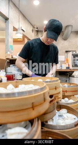 Ein Küchenchef bereitet Xiaolongbao in einer gemütlichen taiwanesischen Restaurantküche akribisch zu. Ein Stapel von Bambusdampfern, gefüllt mit frisch zubereiteten Teigtaschen, kann einzeln verwendet werden Stockfoto