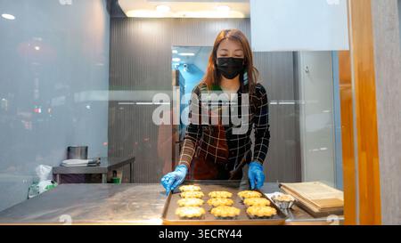 Ein Bäcker in einer taiwanesischen Bäckerei in Taipeh präsentiert ein Tablett mit frisch gebackenen Eierkörtchen. Das einladende Display zeigt das goldene Gebäck und hebt t hervor Stockfoto