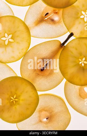 Draufsicht der durchscheinenden Birnenhälften und Apfelscheiben, die als sich wiederholendes Muster auf einem hellen weißen Hintergrund angeordnet sind und Samen, Stieldetails, A hervorheben Stockfoto