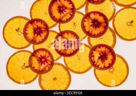 Blick von oben auf helle Zitrusscheiben, die einen frischen Hintergrund bilden, mit orangefarbenen und blutorangen Runden mit leuchtend roten Mittelpunkten, ideal für den Sommer, f Stockfoto