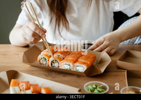 Eine Person genießt an einem freien Tag zu Hause eine köstliche Sushi-Mahlzeit und nimmt mit Stäbchen verschiedene Sushi-Brötchen in einer gemütlichen und entspannten Atmosphäre, Highlight Stockfoto