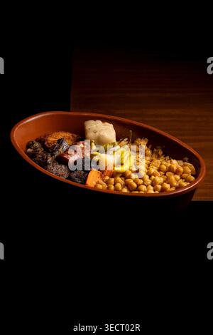 Eine herzhafte Portion traditioneller spanischer Cocido, serviert in einem rustikalen Tontopf. Dieses wohltuende Gericht ist gefüllt mit Kichererbsen, verschiedenen Fleischsorten und Gemüse Stockfoto