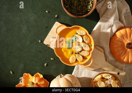 Eine Schüssel cremige Kürbissuppe, garniert mit Croutons, frischen Kräutern und Samen, auf dunkelgrünem Hintergrund. Perfektes Herbstessen, das essen verkörpert Stockfoto