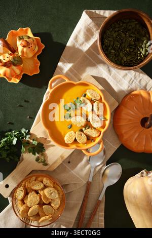 Cremige Kürbissuppe garniert mit knusprigen Croutons, Samen und frischen Kräutern, serviert in einer Kürbisform auf dunkelgrünem Hintergrund, die das e einfängt Stockfoto