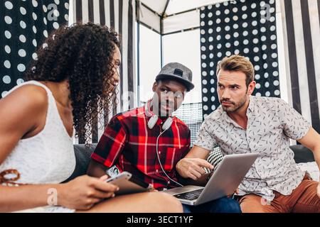 Drei junge Erwachsene arbeiten in einem modernen Café zusammen, lesen Notizen und einen Laptop-Bildschirm, während sie Ideen für ein Startup-Projekt, Teamwork, A diskutieren Stockfoto