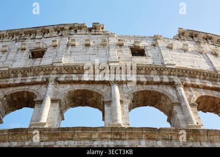 Detaillierter Blick auf die alte römische Kolosseum-Fassade in Rom, mit verwitterten Steinbögen und klassischer Architektur unter einem klaren blauen Himmel, einem fa Stockfoto