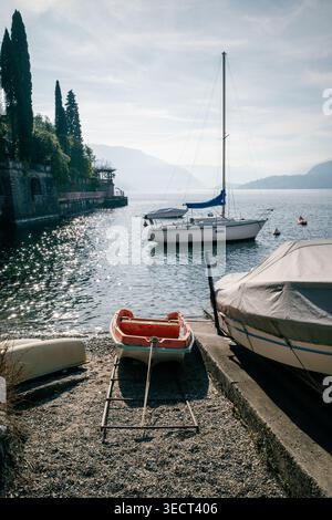 Eine malerische europäische Seeszene mit verankerten Segelbooten und einem Ruderboot an einem sonnigen, ruhigen Tag. Smaragdbäume und Berge bereichern die Landschaft Stockfoto