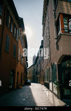 Eine enge europäische Straße mit warmem Sonnenlicht, flankiert von historischen Gebäuden. Der hoch aufragende Glockenturm im Hintergrund rundet das malerische, Stockfoto
