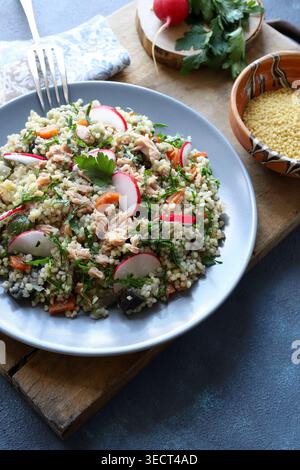 Gesunder mediterraner Couscous-Salat mit Thunfisch, frischem Rettich und Petersilie auf einem rustikalen Holzbrett. Couscous Tabbouleh. Mediterranes Ernährungskonzept. Stockfoto