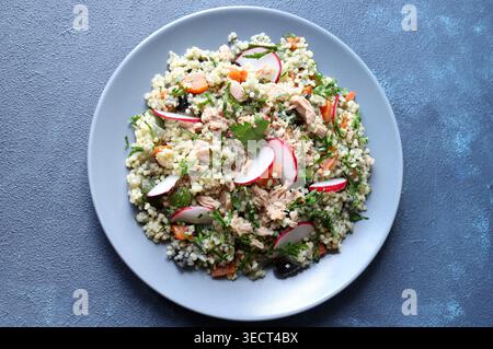 Gesunder mediterraner Couscous-Salat mit Thunfisch, frischem Rettich und Petersilie auf blauem Hintergrund. Couscous Tabbouleh. Mediterranes Ernährungskonzept. Stockfoto