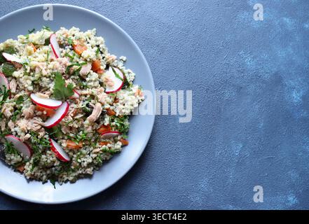 Gesunder mediterraner Couscous-Salat mit Thunfisch, frischem Rettich und Petersilie auf blauem Hintergrund. Couscous Tabbouleh. Mediterranes Ernährungskonzept. Stockfoto
