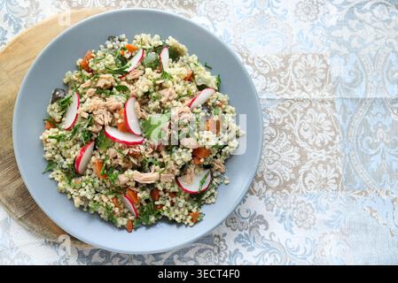 Gesunder mediterraner Couscous-Salat mit Thunfisch, frischem Rettich und Petersilie auf beigem Damastmuster auf Stoffhintergrund. Hausgemachte Couscous Tabbouleh. Stockfoto