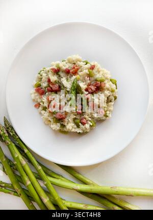 Nahaufnahme eines Gourmet-Spargels und knusprigem Speckrisotto, serviert auf einem modernen Teller. Helle, luftige Lebensmittelfotografie mit Frühlingsmotiven. Draufsicht. Stockfoto
