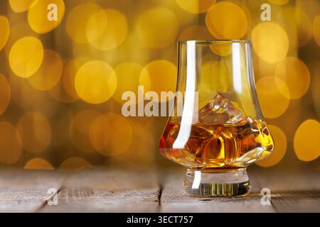 Whiskey-Glas mit goldenem Bernsteinlikör und Eiswürfeln auf rustikaler Holzoberfläche mit verschwommenem Bokeh-Hintergrund Stockfoto