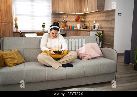 Wettbewerbsfähige Frau mit kabellosen Kopfhörern, die zu Hause Videospiele spielt. Stockfoto