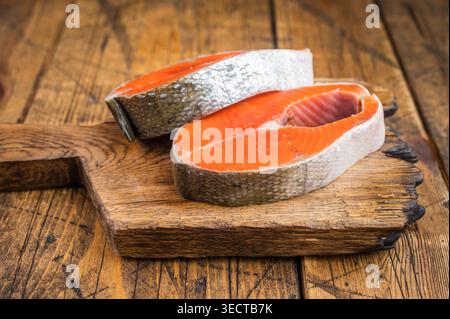 Rohe Lachssteaks mit Haut und Knochen an Bord mit Kräutern und Zitrone, natürlicher Holzhintergrund mit Kopierraum Stockfoto