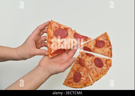 Mit zwei Händen werden die Scheiben einer Peperoni-Pizza auseinander gezogen, um den käsigen Stretch zu zeigen. Die Hand nimmt ein Stück von einer Pizza auf, mit einem Stück Käse, das sich dehnt Stockfoto