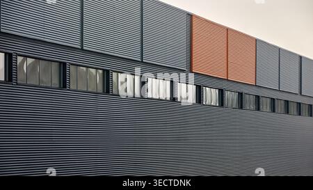 Architektonische Fassade mit orangen Fassaden, gewellte Metallpaneele, großes Glasfenster eines Industrie- oder Geschäftsgebäudes, zeitgenössische Architektur Stockfoto