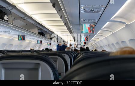 Innenraum einer gewerblichen Flugzeugkabine mit Flugbegleitern im Gang und Sitzplätzen. Moderne Flugzeuge mit Überdachungsfächern und Schirmen. Stockfoto